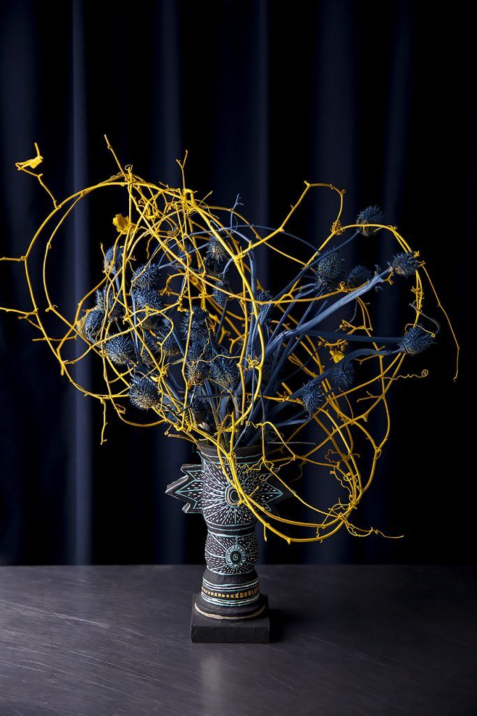 a vase filled with yellow branches on top of a wooden table next to a blue curtain