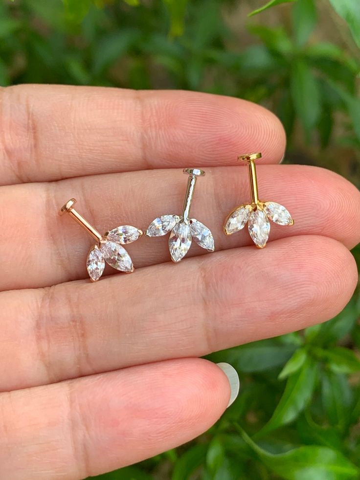 a person is holding three pairs of ear studs in their left hand and one has two small diamond leaves on it