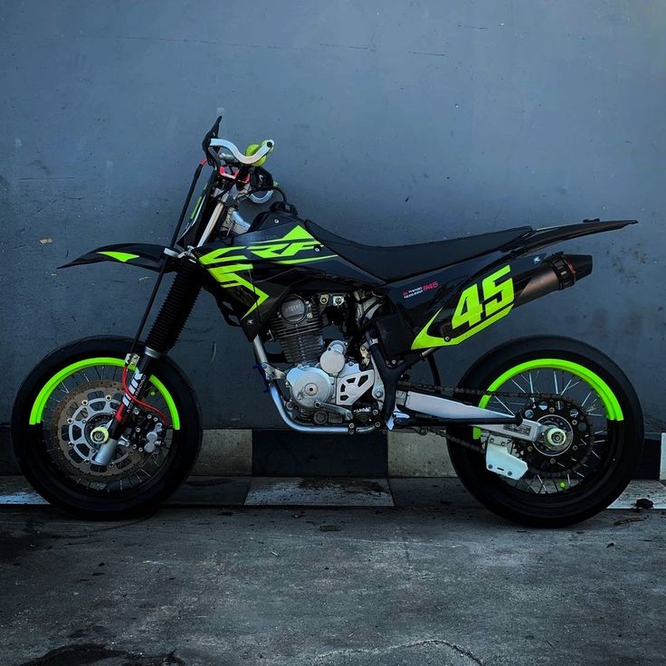 a black and yellow dirt bike parked in front of a gray wall with neon green accents