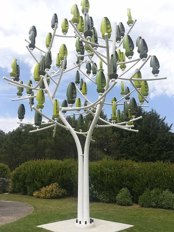 a white sculpture with green leaves on it's branches in front of some bushes