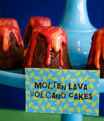 chocolate lava cakes with orange icing on a blue platter and a sign that says molten lava volcano cakes