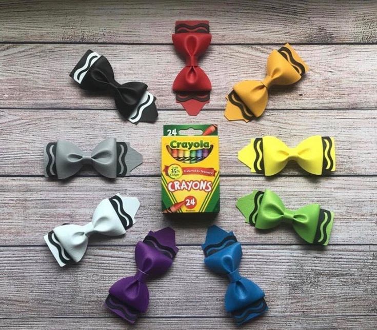 several different colored bow ties laid out on a wooden table with crayons in the background