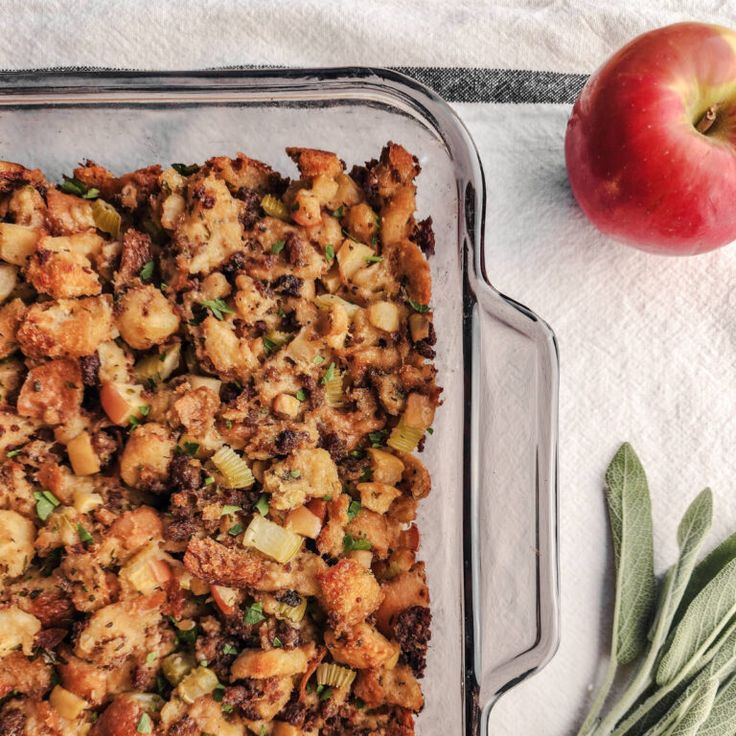 a casserole dish with stuffing next to an apple and sagel on a towel