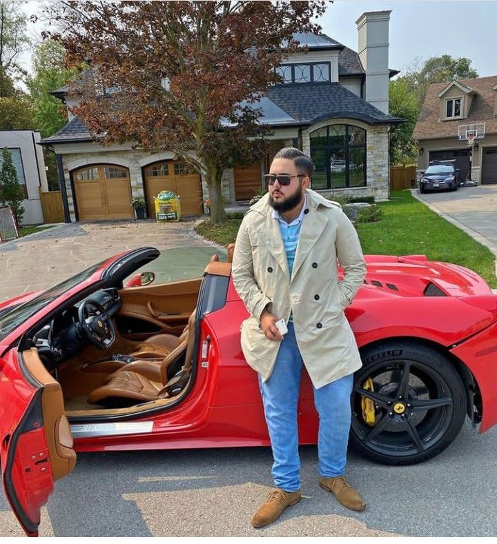 a man standing next to a red sports car in front of a house with the door open