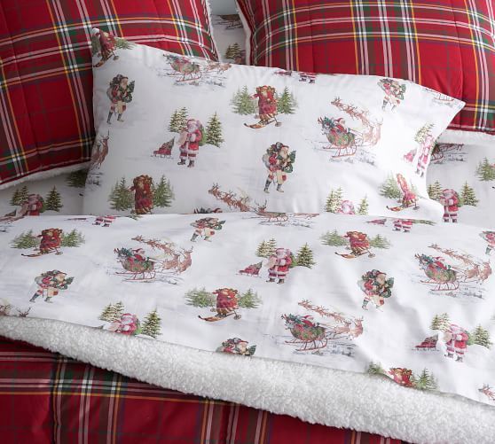 a bed with santa claus on it and plaid comforter in the middle, along with two pillows