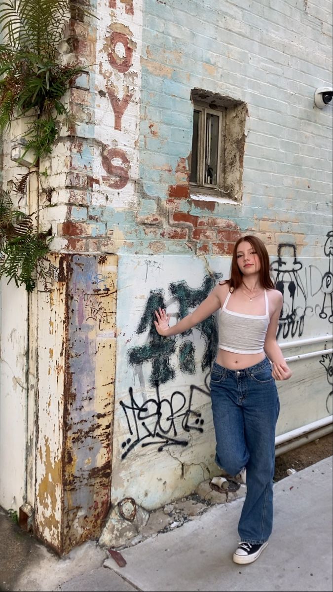 a woman standing next to a building with graffiti on the wall and windows in it