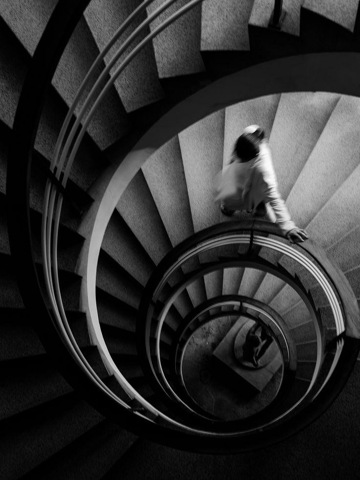 black and white photograph of man walking down spiral staircase