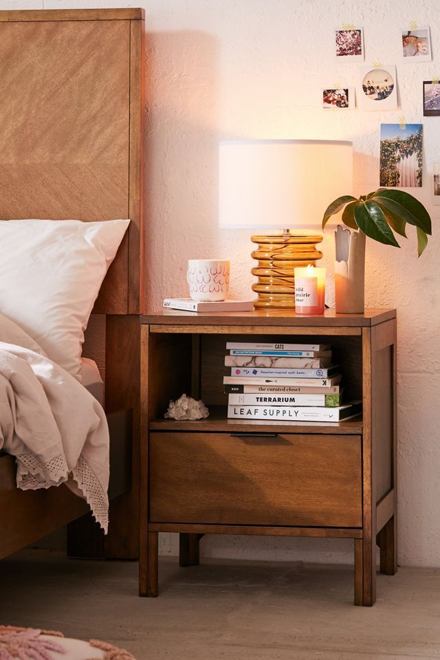 a nightstand with books and candles on it next to a bed in a white bedroom