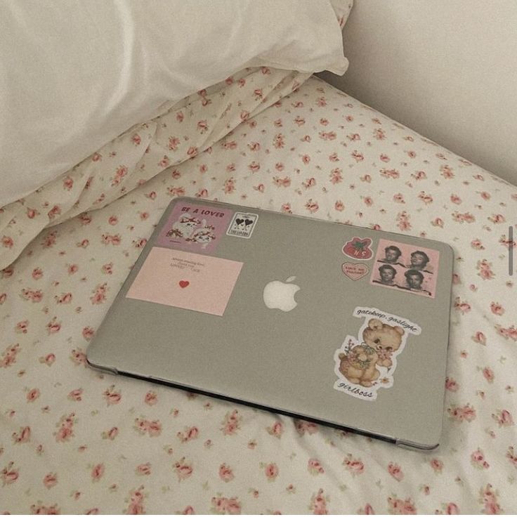 an apple laptop sitting on top of a bed covered in pink and white floral sheets