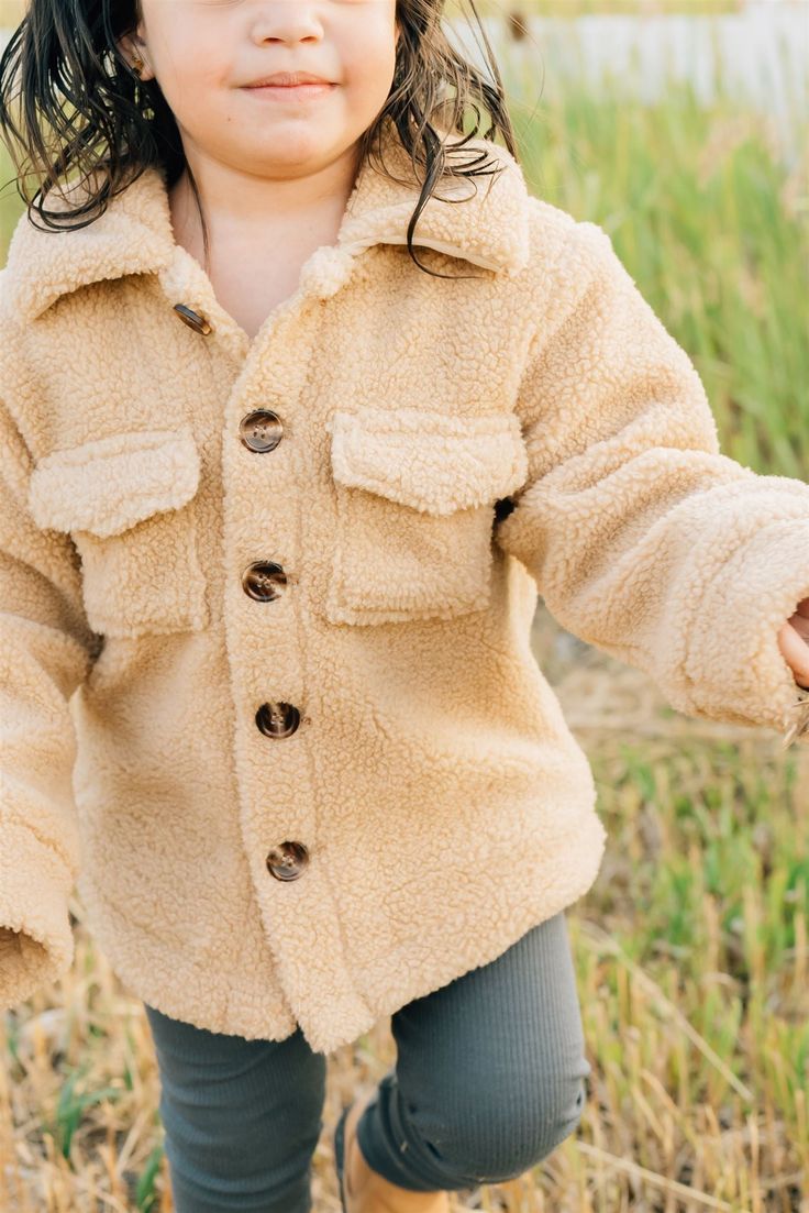 Keep your little one cozy + stylish with the Sherpa Shacket. This adorable shacket is designed for babies + toddlers up to 5T, providing warmth + comfort during chilly days. Made from soft + plush sherpa material, it is gentle on delicate skin. The shacket features a trendy design that can be easily layered over any outfit, making it a versatile addition to your child's wardrobe. 100% Cotton Wash in cold water, Tumble dry low. Runs oversized, size down one size! Length: 0-3m 11, 3-6m 11.75, 6-12 Cute Cream Winter Outerwear, Cute Cream Outerwear, Casual Warm Outerwear For Playtime, Casual Winter Outerwear For Playtime, Cute Cream Long Sleeve Outerwear, Cute Fall Outerwear With Buttons, Cozy Beige Shacket For Winter, Cute Warm Long Sleeve Outerwear, Cute Long Sleeve Warm Outerwear