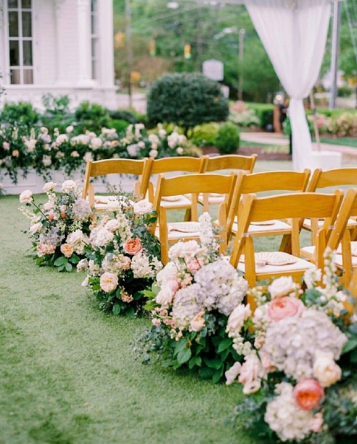 rows of wooden chairs lined up with flowers and greenery in front of a building