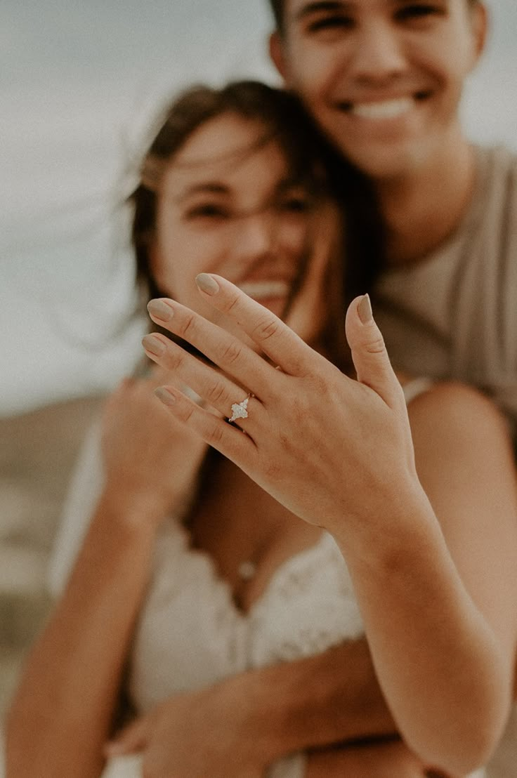 a man and woman are smiling while holding their hands up to show the engagement ring