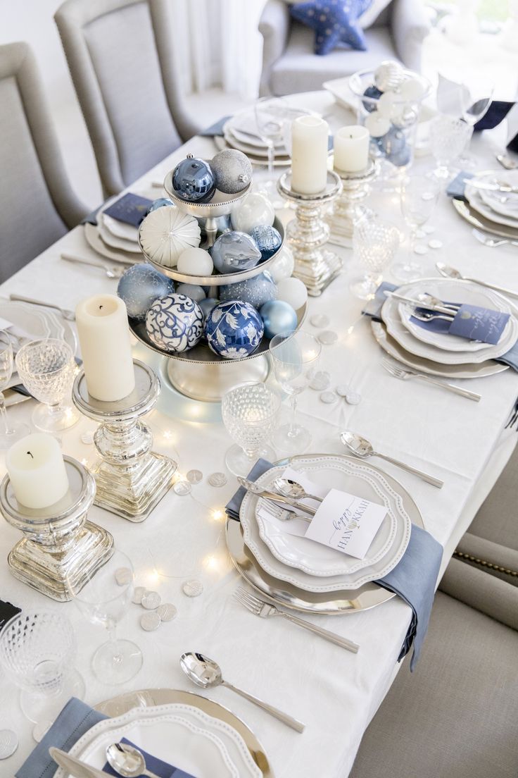 the table is set with blue and white dishes, silverware, candles, and napkins