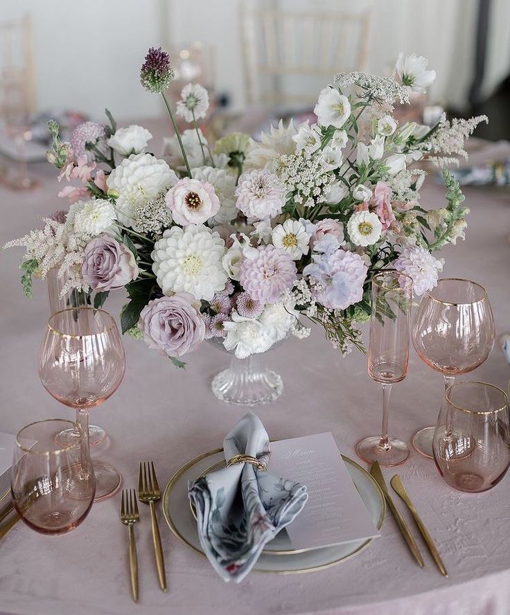 the table is set with pink and white flowers in vases, silverware, and napkins