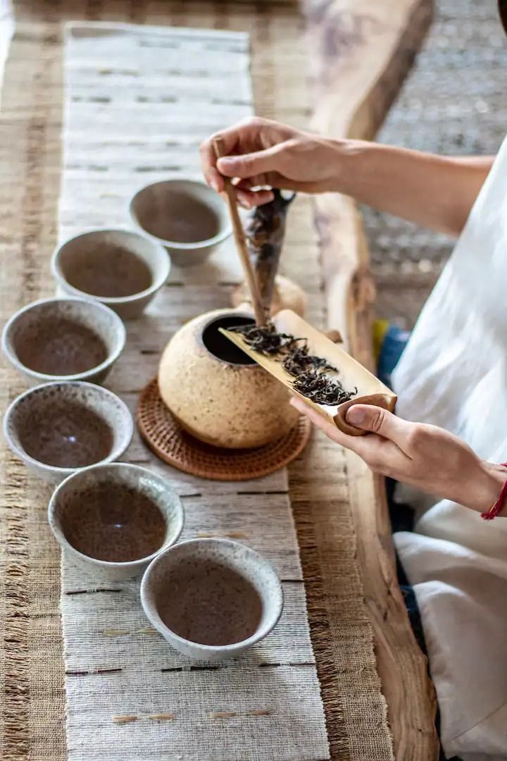 a woman is preparing some food on a wooden table with many bowls and spoons