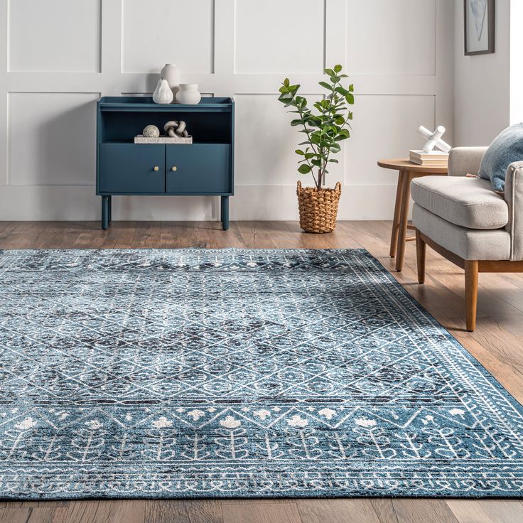 a blue area rug with an ornate design on the floor and sideboard in the background