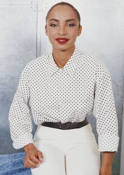 a woman in white pants and a polka dot shirt is posing for a photo with her hands on her hips