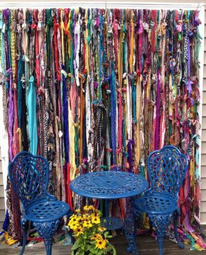 two blue chairs sitting next to each other near a table and chair covered in scarves