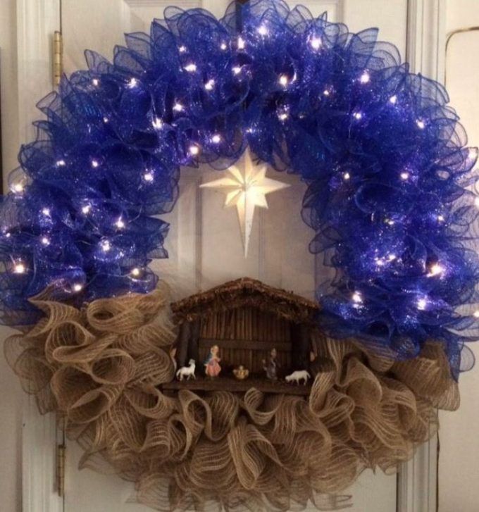 a nativity wreath hanging on the front door with blue lights and decorations around it