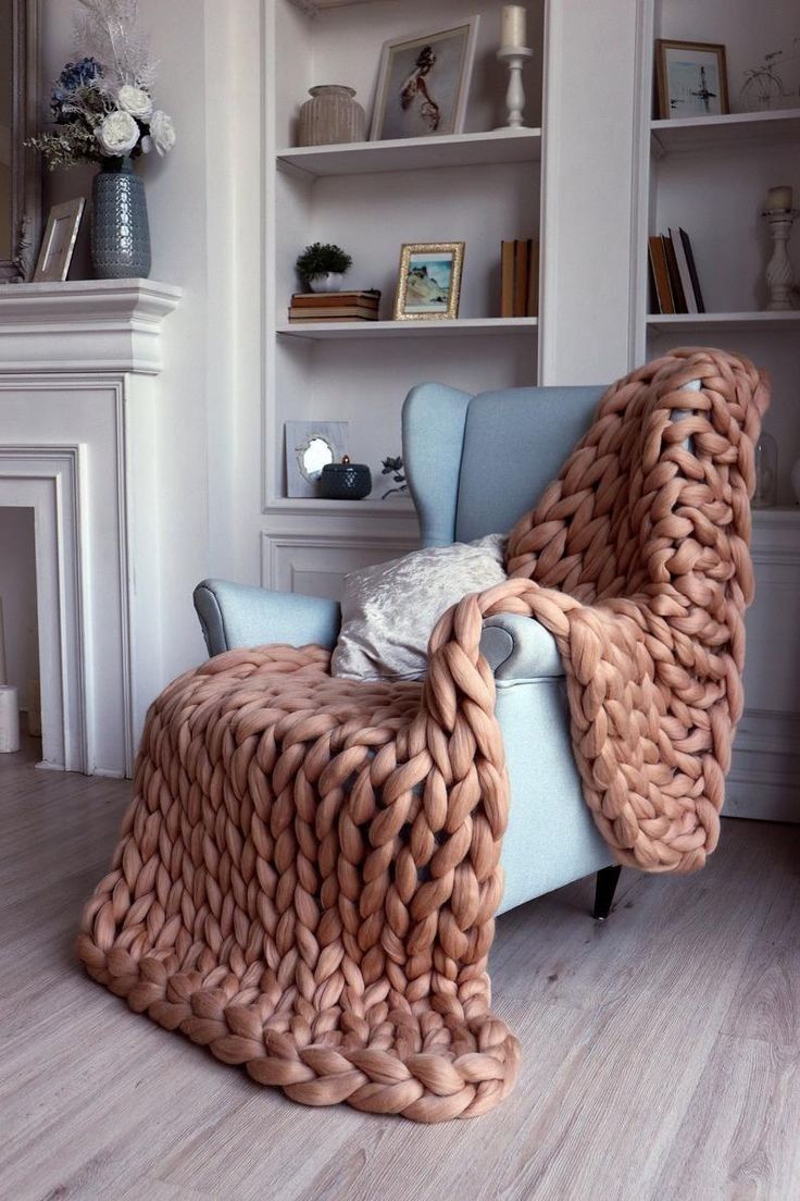 a large chunky blanket sitting on top of a blue chair in front of a fireplace