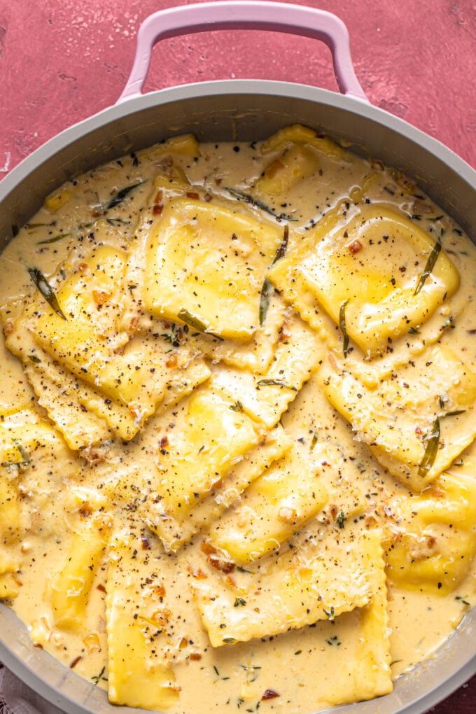 a pan filled with ravioli and sauce on top of a red tablecloth next to a spoon