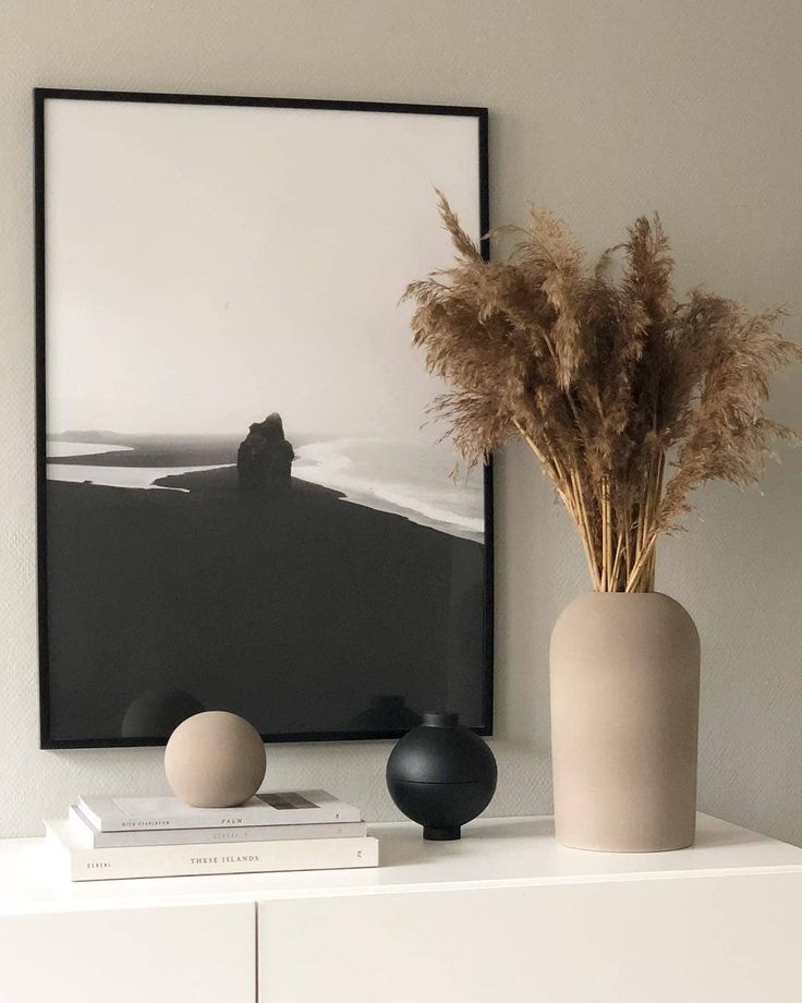 two vases with dry grass in them sit on a shelf next to an art print