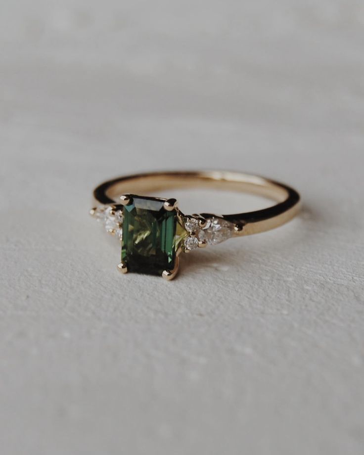 a gold ring with a green stone and three diamonds on the side, sitting on a white surface