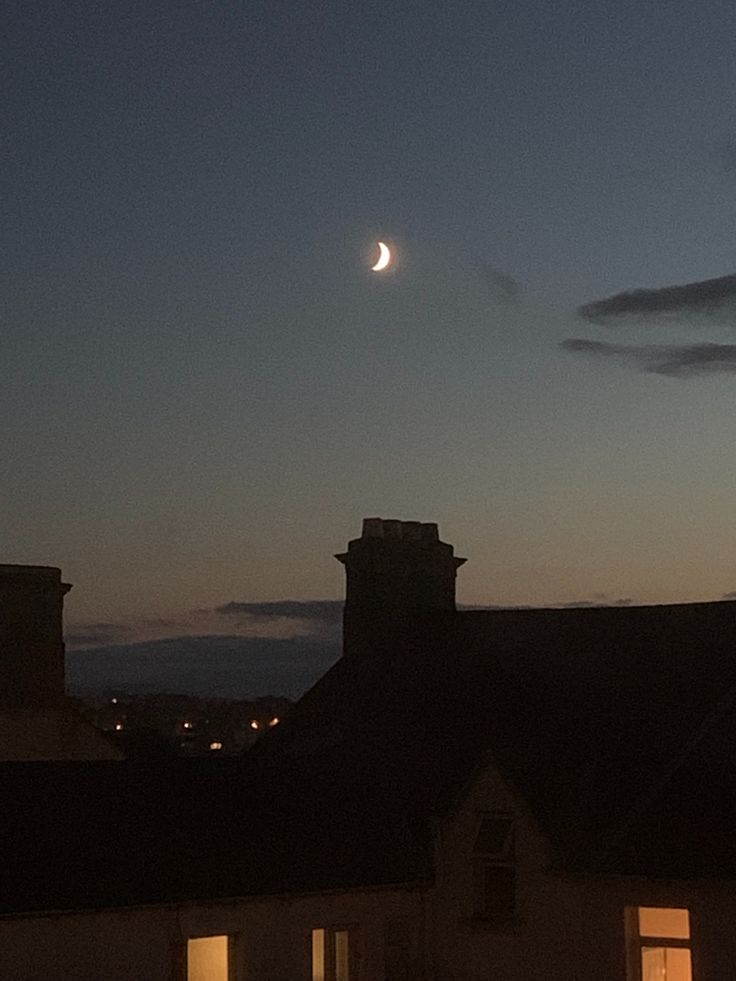 the moon is shining brightly in the night sky over some rooftops and buildings with windows