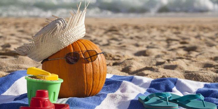 a pumpkin with sunglasses and hat sitting on a towel at the beach