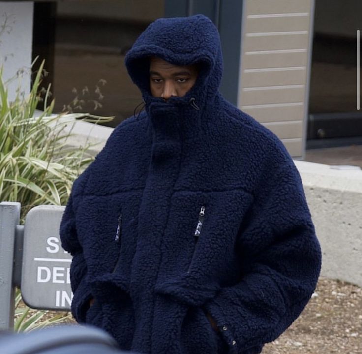 a man in a blue jacket is walking down the street with his hand on his hip