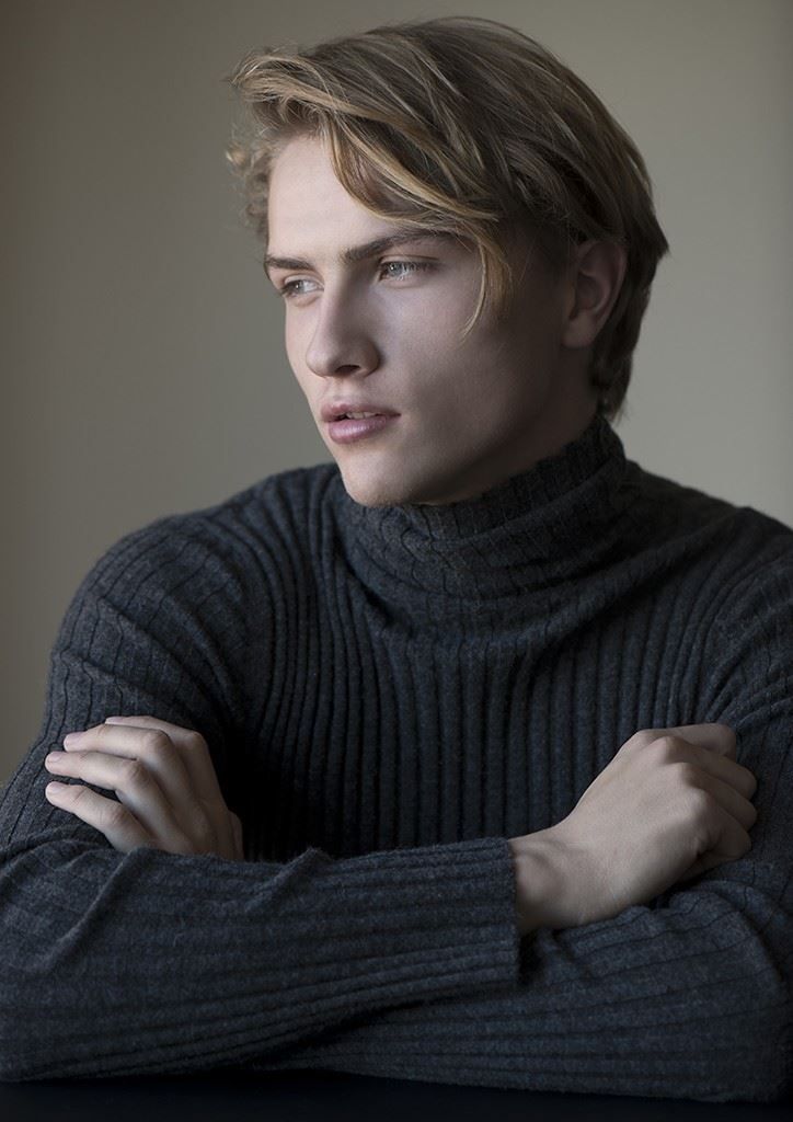 a young man with his arms crossed sitting at a table in front of a window