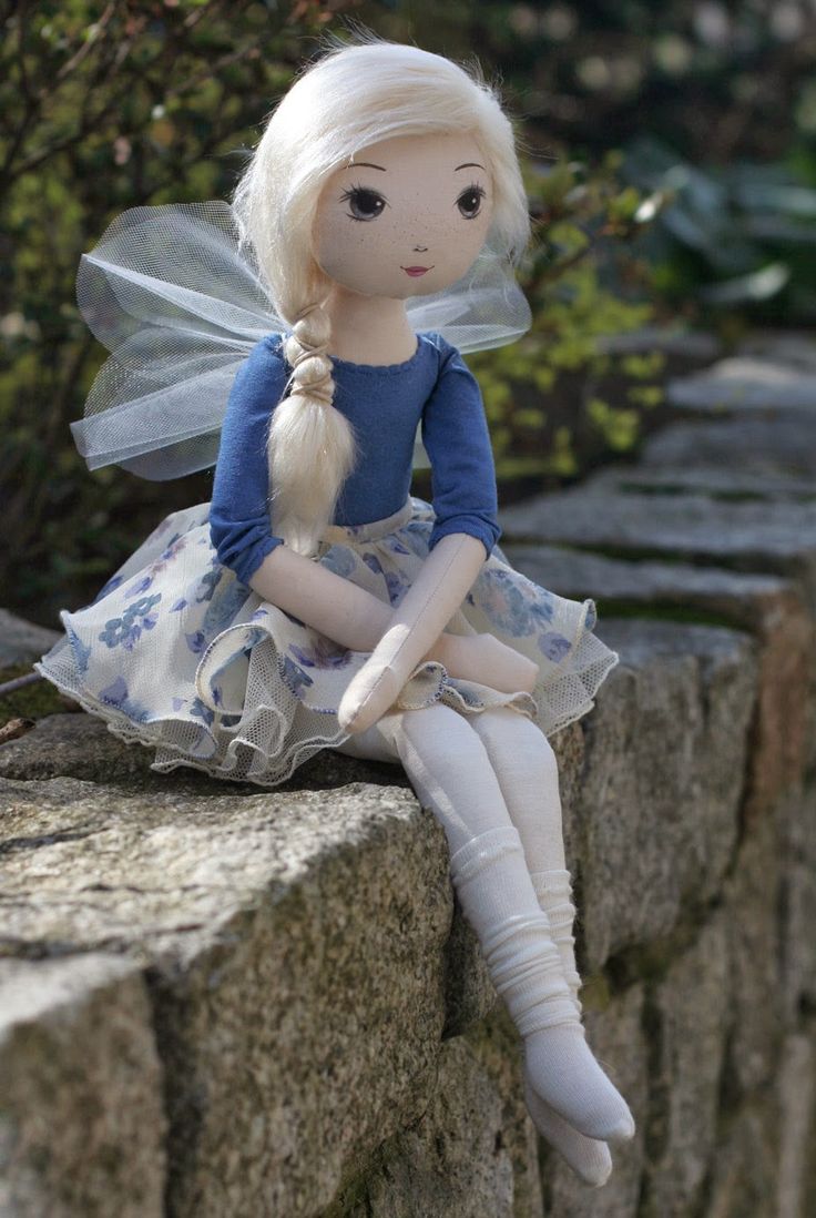 a doll sitting on top of a stone wall wearing a blue dress and white tights