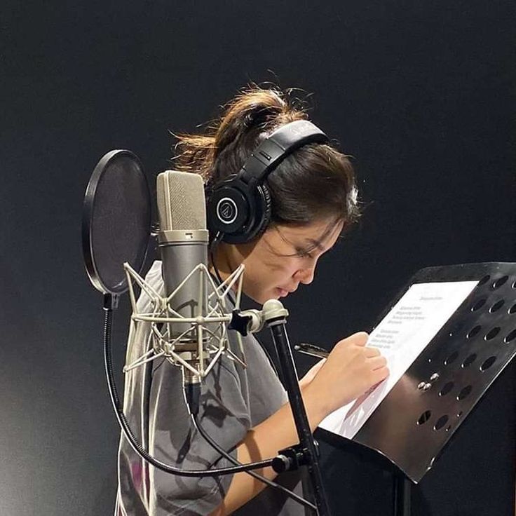 a woman with headphones on reading a piece of paper in front of a microphone