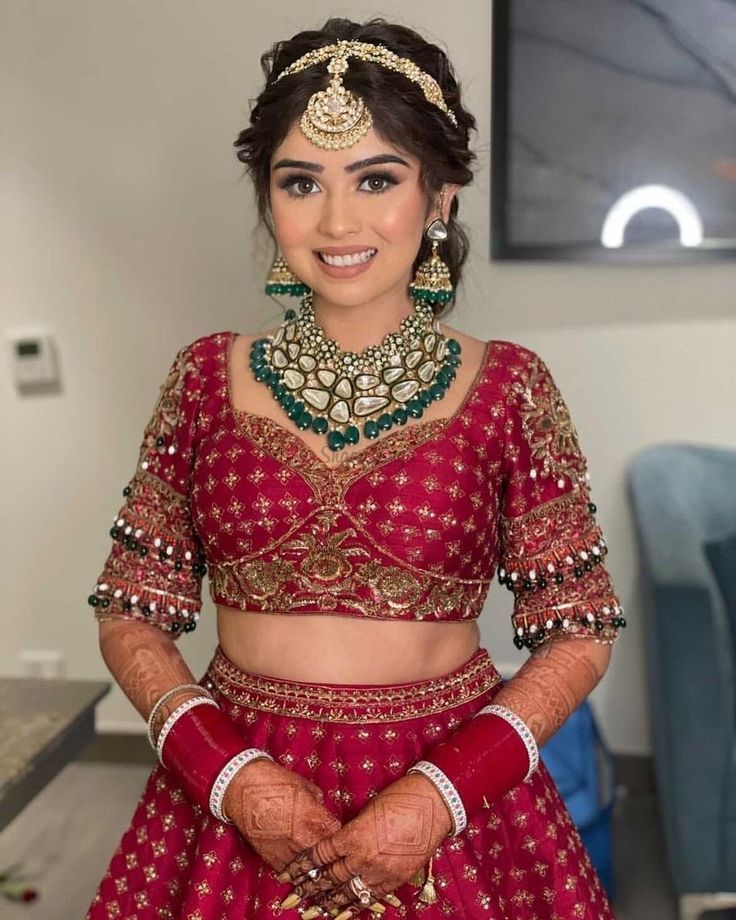 a woman in a red lehenga and matching jewelry is posing for the camera