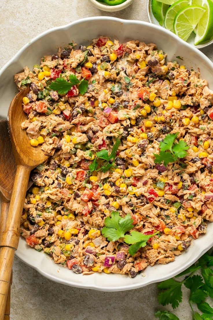 mexican rice salad in a white bowl with a wooden spoon and limes on the side