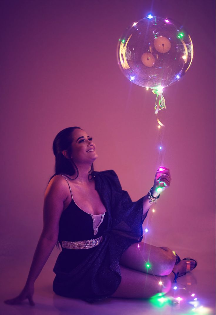 a woman sitting on the floor with a balloon in her hand and some lights around her