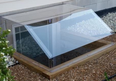 a glass box sitting on top of a gravel ground next to a planter filled with flowers