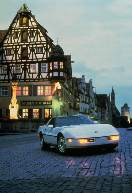 a white sports car parked in front of a large building at night with lights on