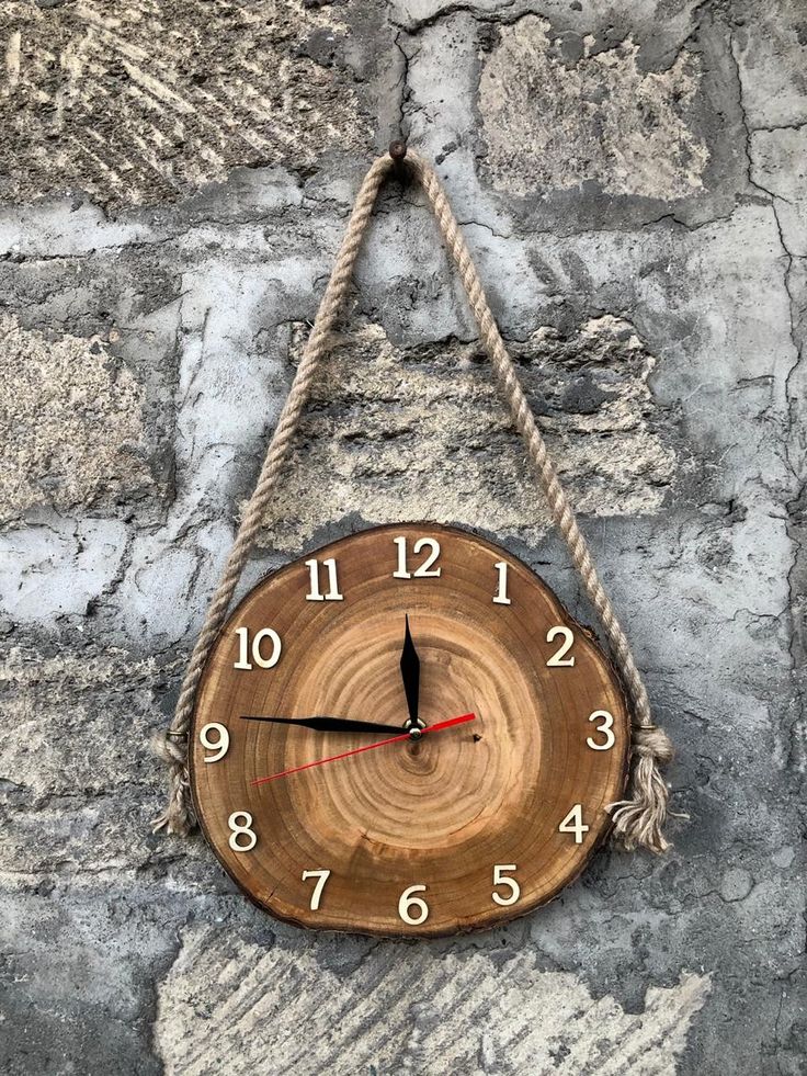 a wooden clock hanging from a rope on a stone wall