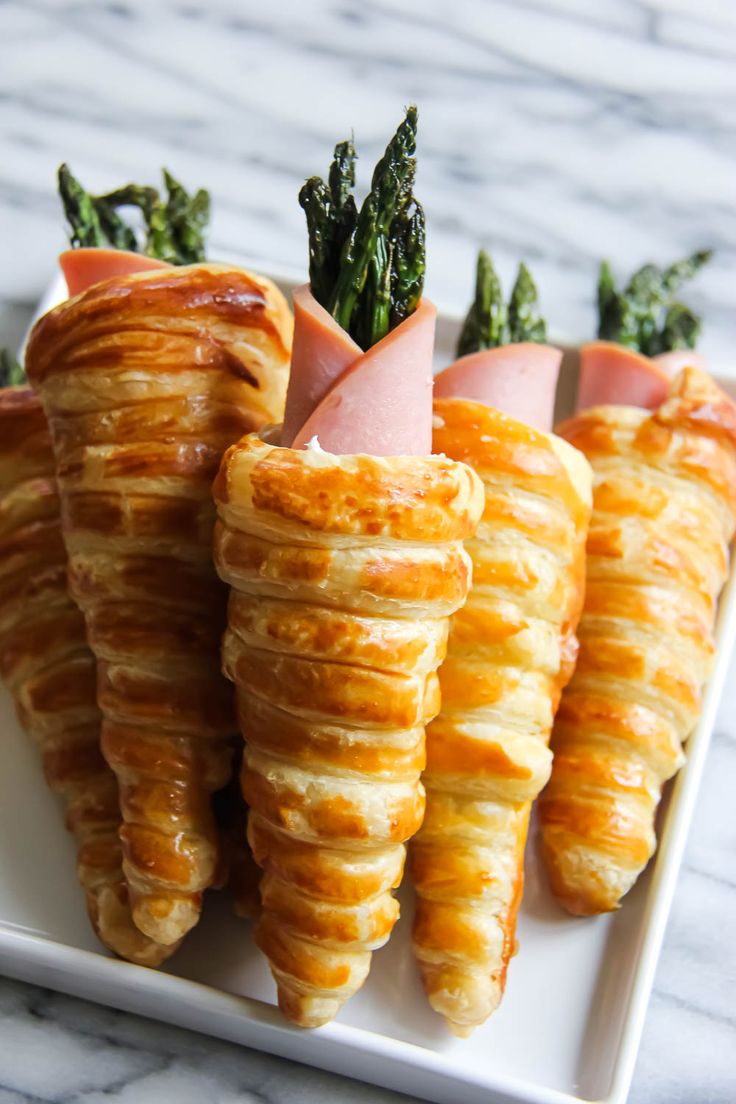 four pieces of food on a white plate with asparagus and ham in the middle