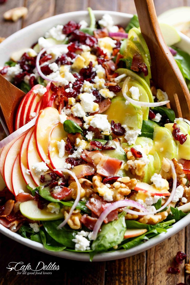 a salad with apples, cranberries, nuts and feta cheese in a white bowl