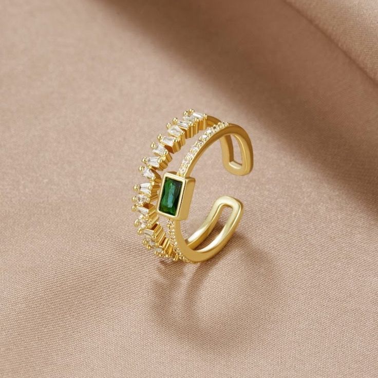 Timeless. Classic. Elegant. Add a touch of luxury to your everyday wardrobe with this stunning ring. Guaranteed to elevate any look. 18K gold-plated Green cubic zirconia crystal Adjustable ring size - one size fits all Hypoallergenic, lead & nickel free If you aren't in LOVE with your purchase, please let us know within 30 days of receiving your item, and you'll receive a stress-free refund. Elegant Adjustable Open Emerald Ring, Elegant Adjustable Gold Emerald Ring, Gold Crystal Ring With Cubic Zirconia Open Design, Gold Cubic Zirconia Open Ring, Elegant Open Emerald Ring With Cubic Zirconia, Elegant Gold Crystal Ring With Sparkling Stones, Elegant Gold Plated Open Crystal Ring, Gold Emerald Open Ring With Vs Clarity, Gold Emerald Ring With Vs Clarity