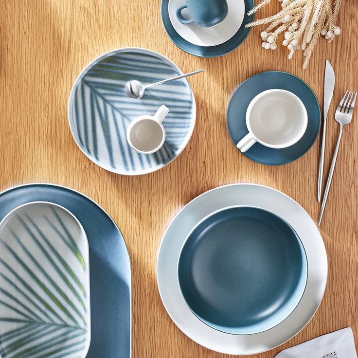 a wooden table topped with blue and white dinnerware on top of a wooden table