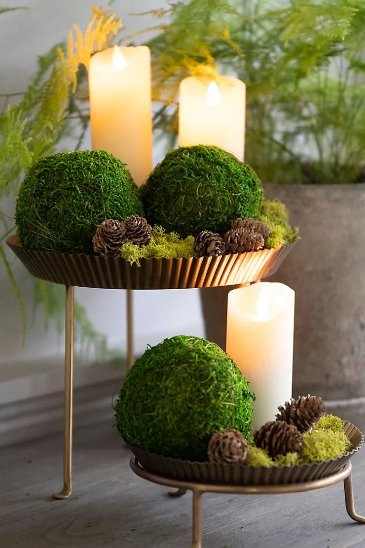 three tiered trays with moss, pine cones and candles in them on a table