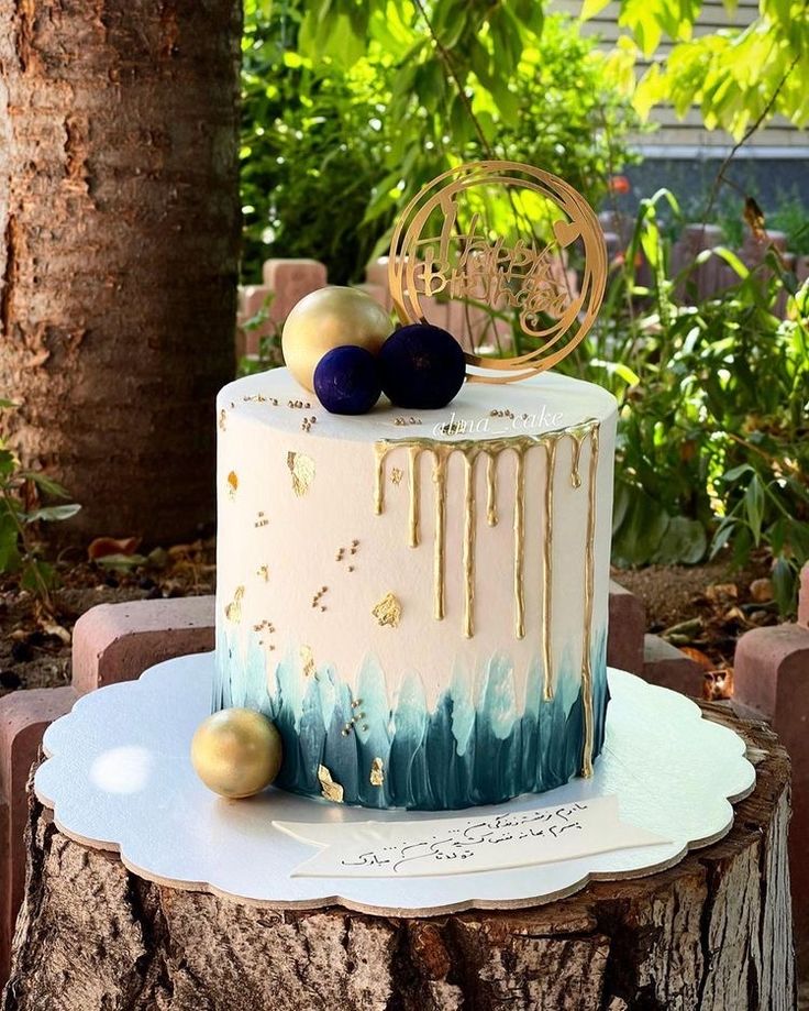 a white and blue cake sitting on top of a wooden table next to a tree