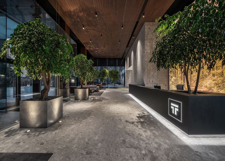 an empty lobby with potted trees in the center and large windows on both sides