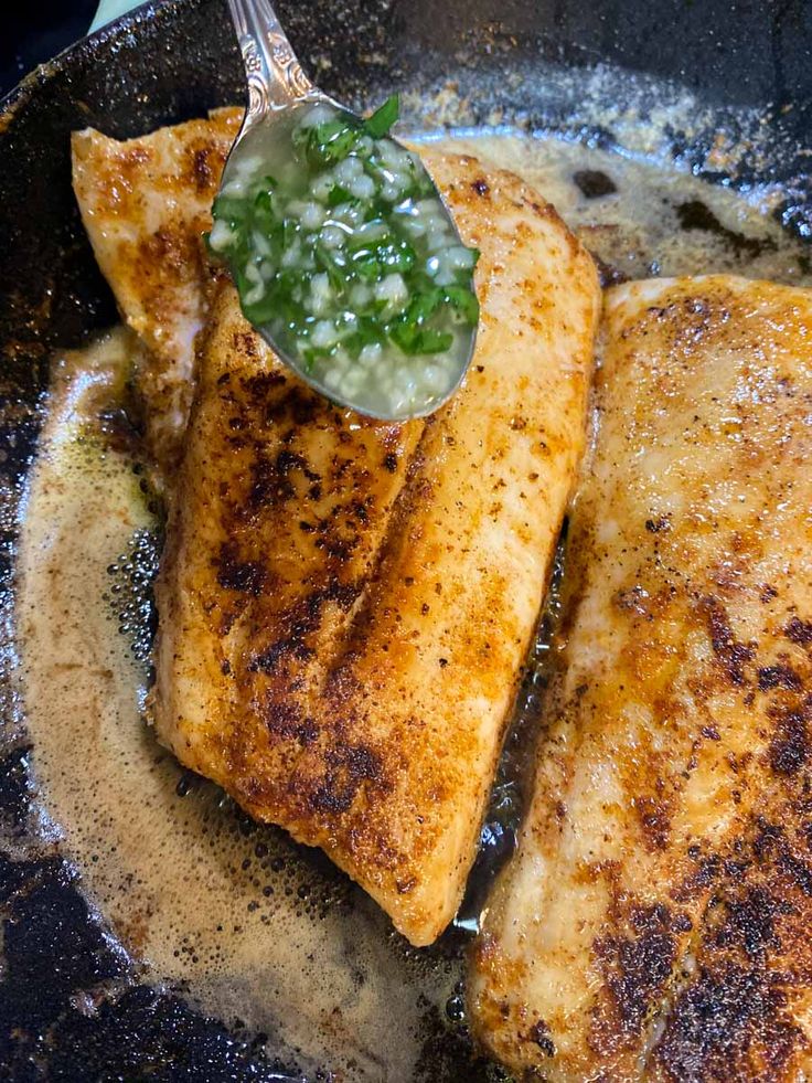 two fish fillets in a frying pan with a green sauce on the side