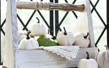 white pumpkins and gourds sit in a wooden crate on a porch railing