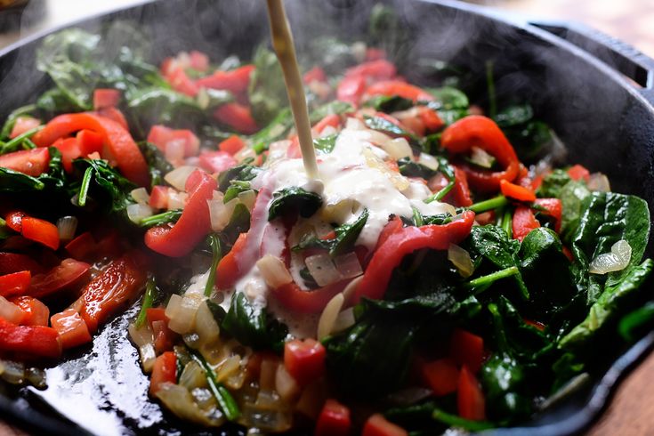 vegetables being cooked in a skillet with a wooden spoon