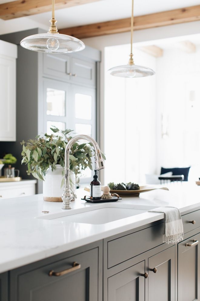 a kitchen with white counter tops and gray cabinets, hanging lights over the island area